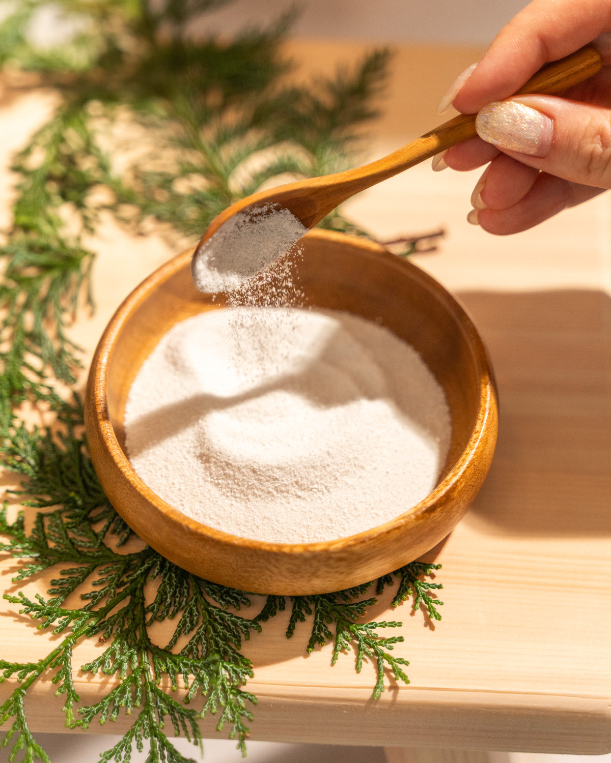 Wooden bowl with white powder and a wooden spoon on a wooden surface with greenery.