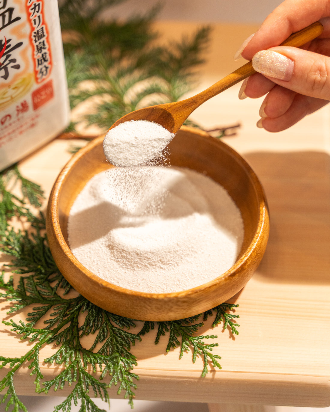 Wooden spoon with white powder over a wooden bowl on a wooden surface with greenery