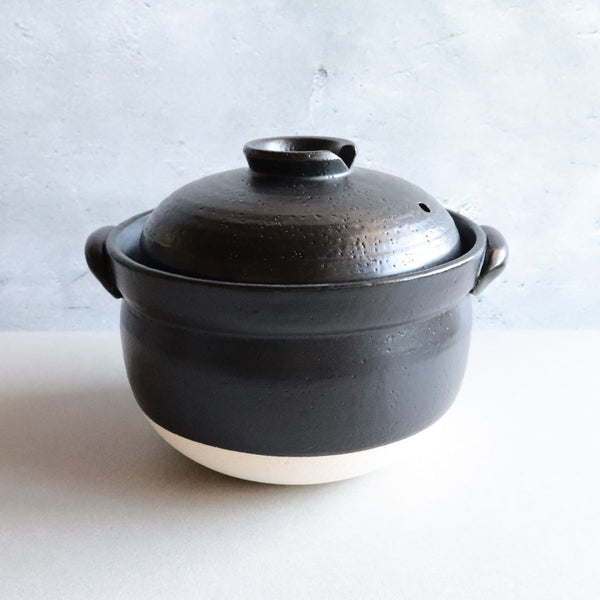 A black glazed donabe rice cooker with its lid on, showcasing its traditional Japanese design. The cooker is made from heat-resistant ceramic and features a sleek, black finish.