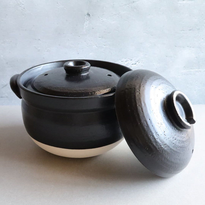 A black glazed donabe rice cooker with the lid partially removed, highlighting the inner cooking pot. The traditional design and heat-retentive material make it perfect for cooking rice.