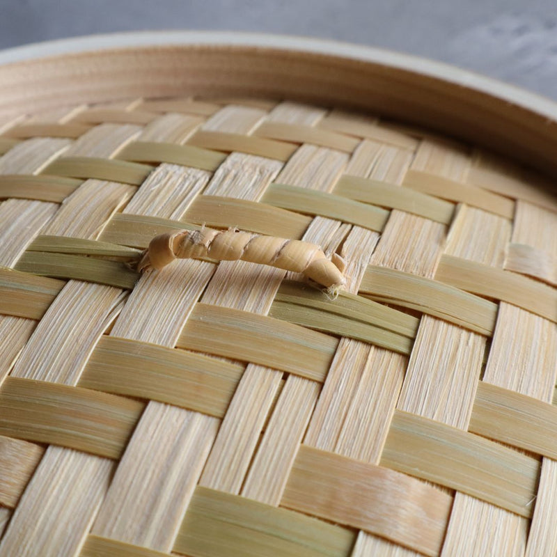 Close-up view of the handle on a woven lid from a Japanese steamer basket, showing intricate bamboo weaving.