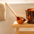 A copper sauna ladle resting on a wooden stool beside a towel, creating a warm and inviting sauna atmosphere.