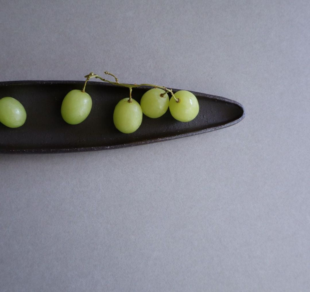 Green grapes on a black oval plate against a gray background
