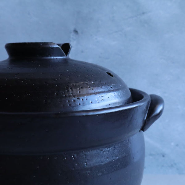 Close-up detail of the lid on a black glazed donabe rice cooker, showing the fine craftsmanship and traditional design. The lid ensures effective heat retention and pressure for perfect rice cooking.