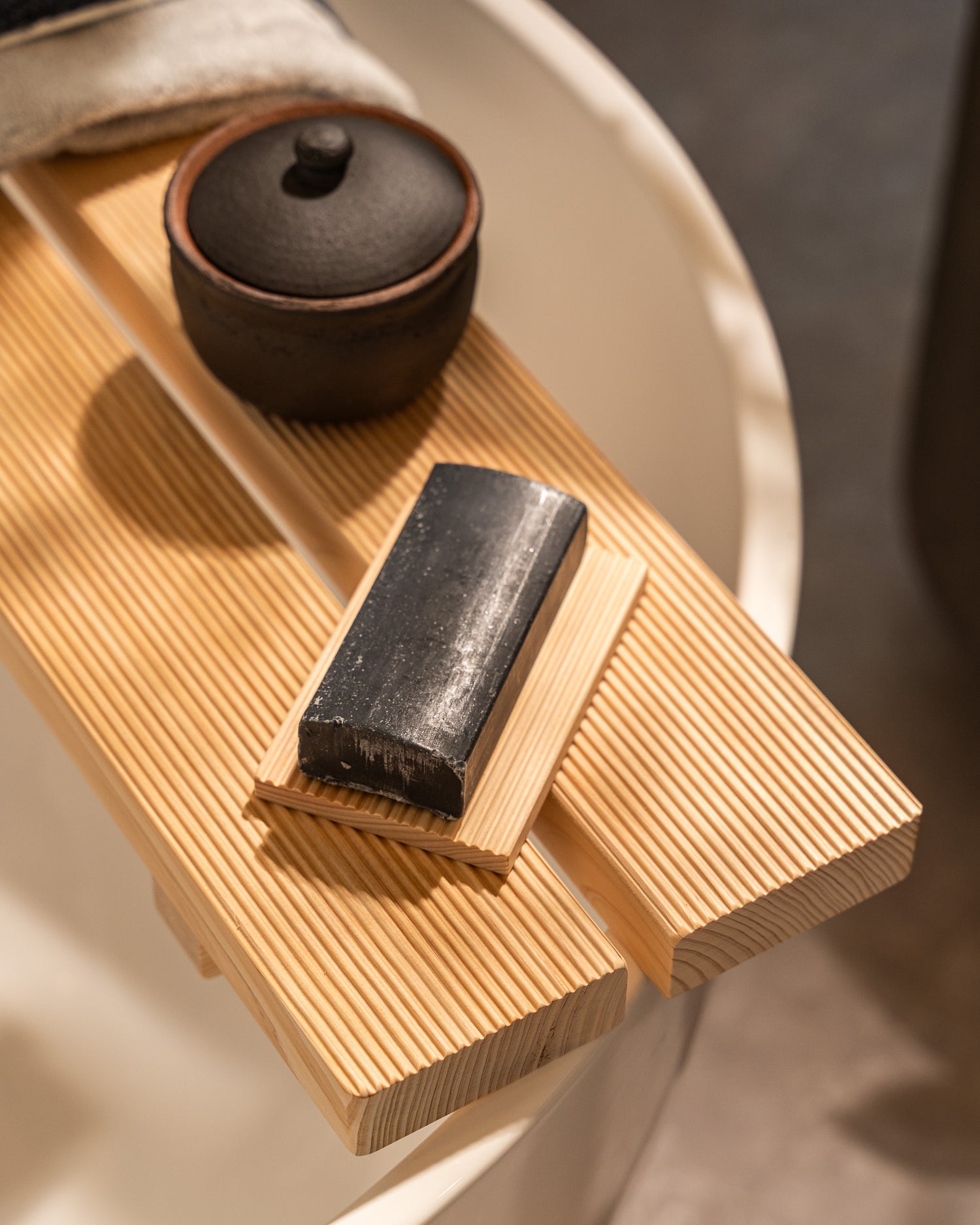 Wooden tray with a black soap bar and small black container on a neutral background