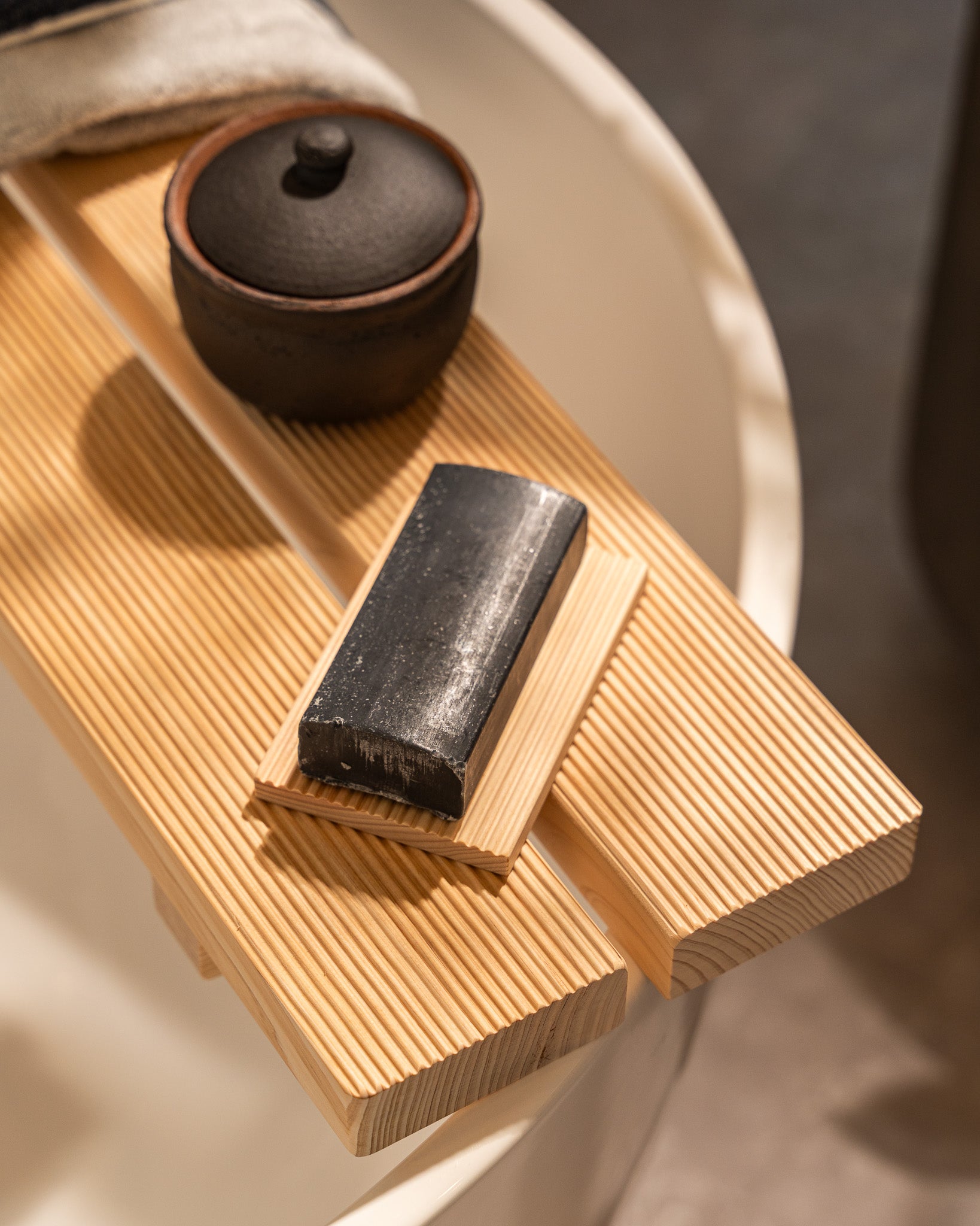 Wooden tray with a black soap bar and small black container on a neutral background
