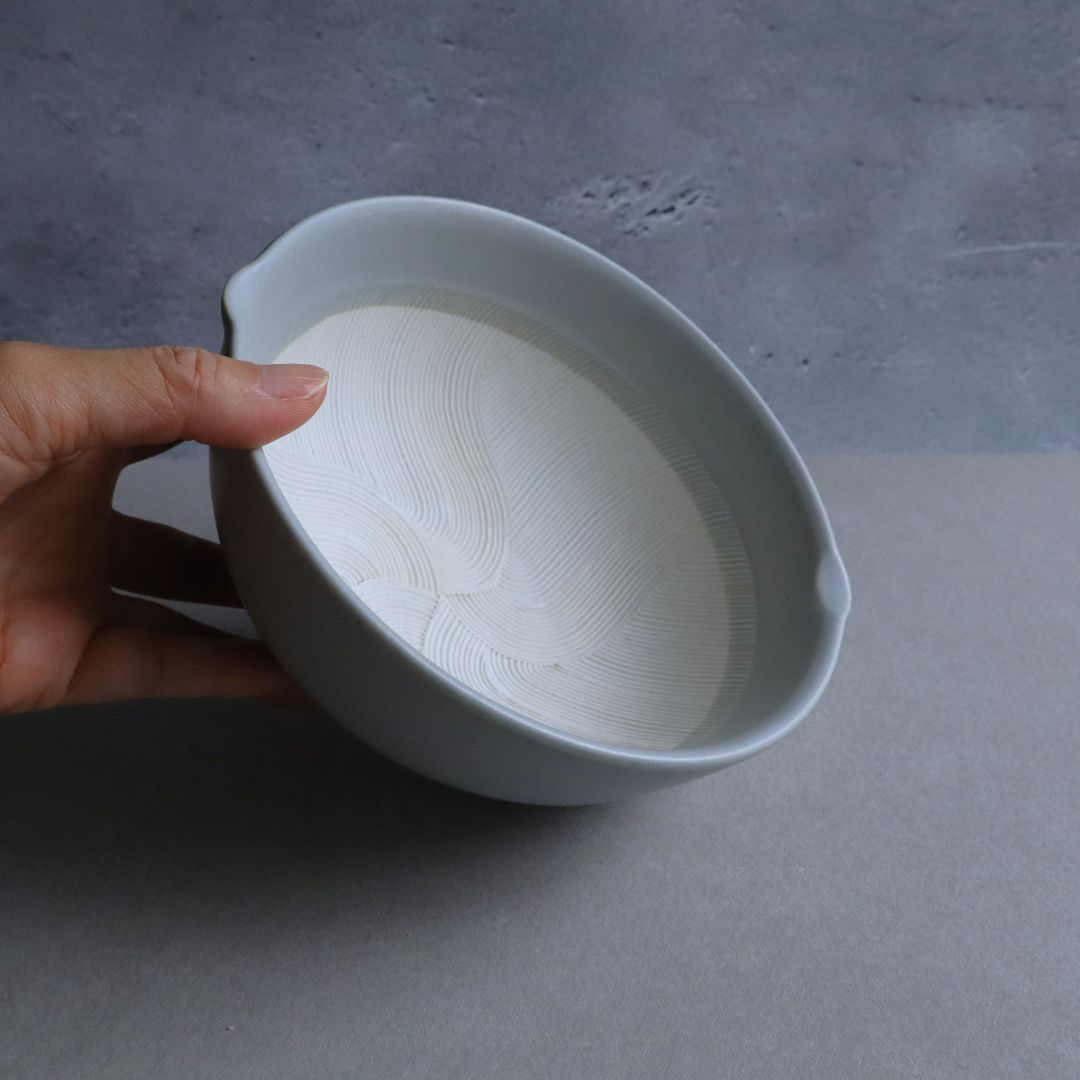 A hand holding the white ceramic suribachi, showing its compact and lightweight design.