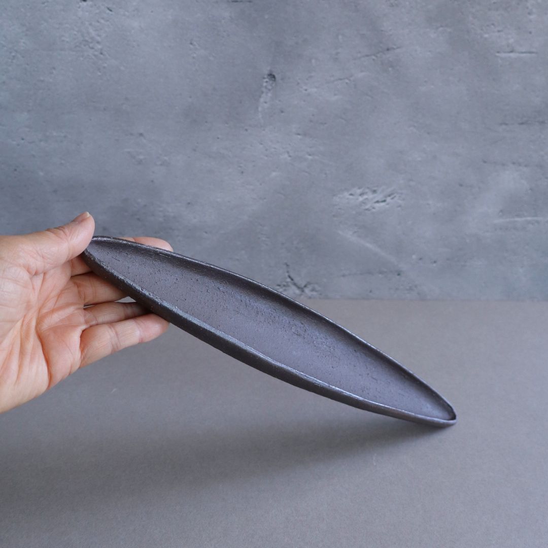 Hand holding a dark gray ceramic plate against a gray background