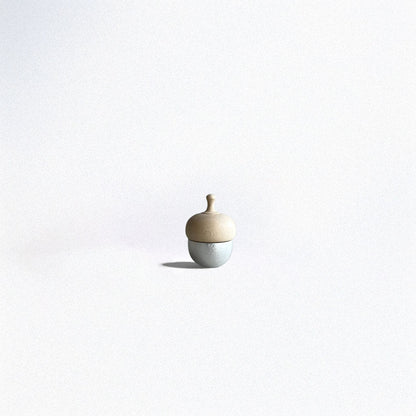A small acorn-shaped healing bell with a silver base and a wooden top, placed on a smooth surface against a soft, neutral background.