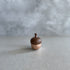 A small acorn-shaped healing bell with a rose gold base and a wooden top, placed on a smooth surface against a soft, neutral background.