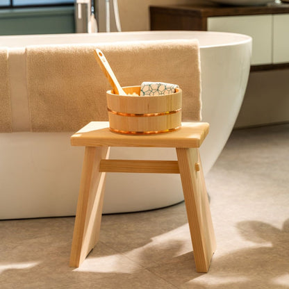 Wooden stool with a basket containing items next to a bathtub in a bathroom setting.