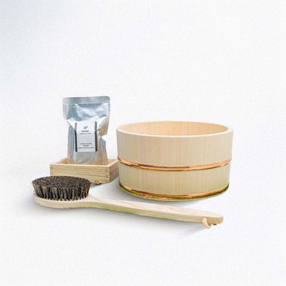 wooden bath bucket and a wooden body brush next to a soap packaging on a white background