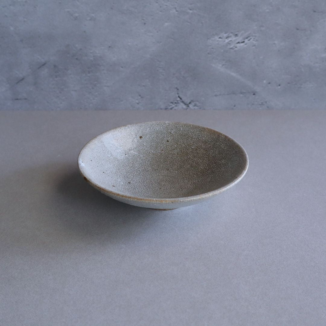 A handmade Japanese ceramic plate with kairagi crackle glaze seen from above, displaying its subtle texture and shallow form.