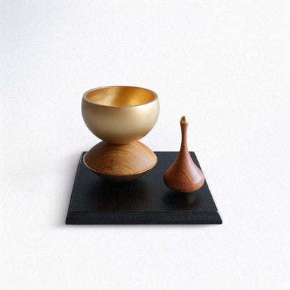 Two wooden bowls, one gold and one brown, on a black square mat with a white background.