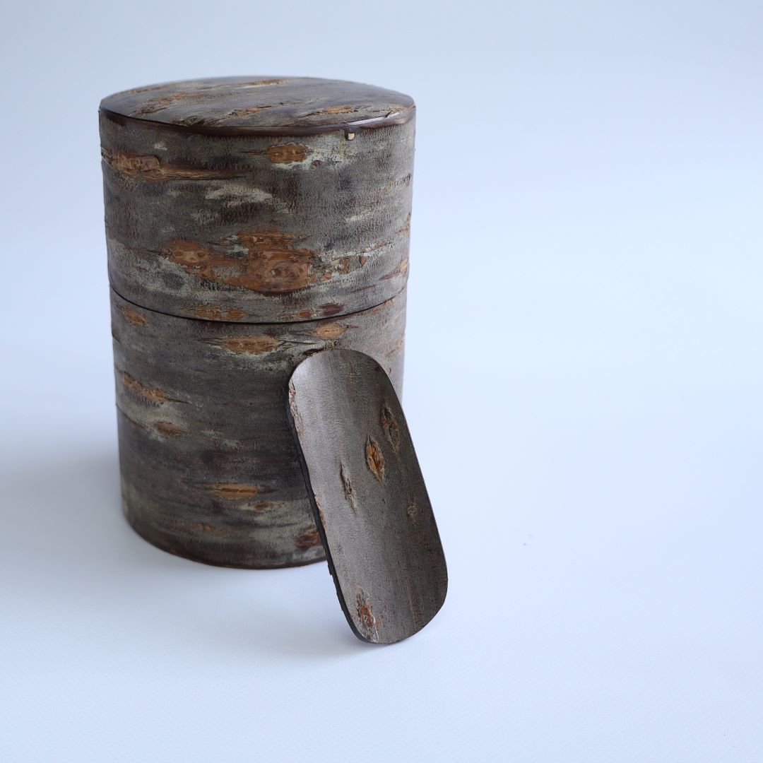 A handcrafted Japanese tea caddy made from cherry bark, featuring a matching scoop displayed next to the caddy.