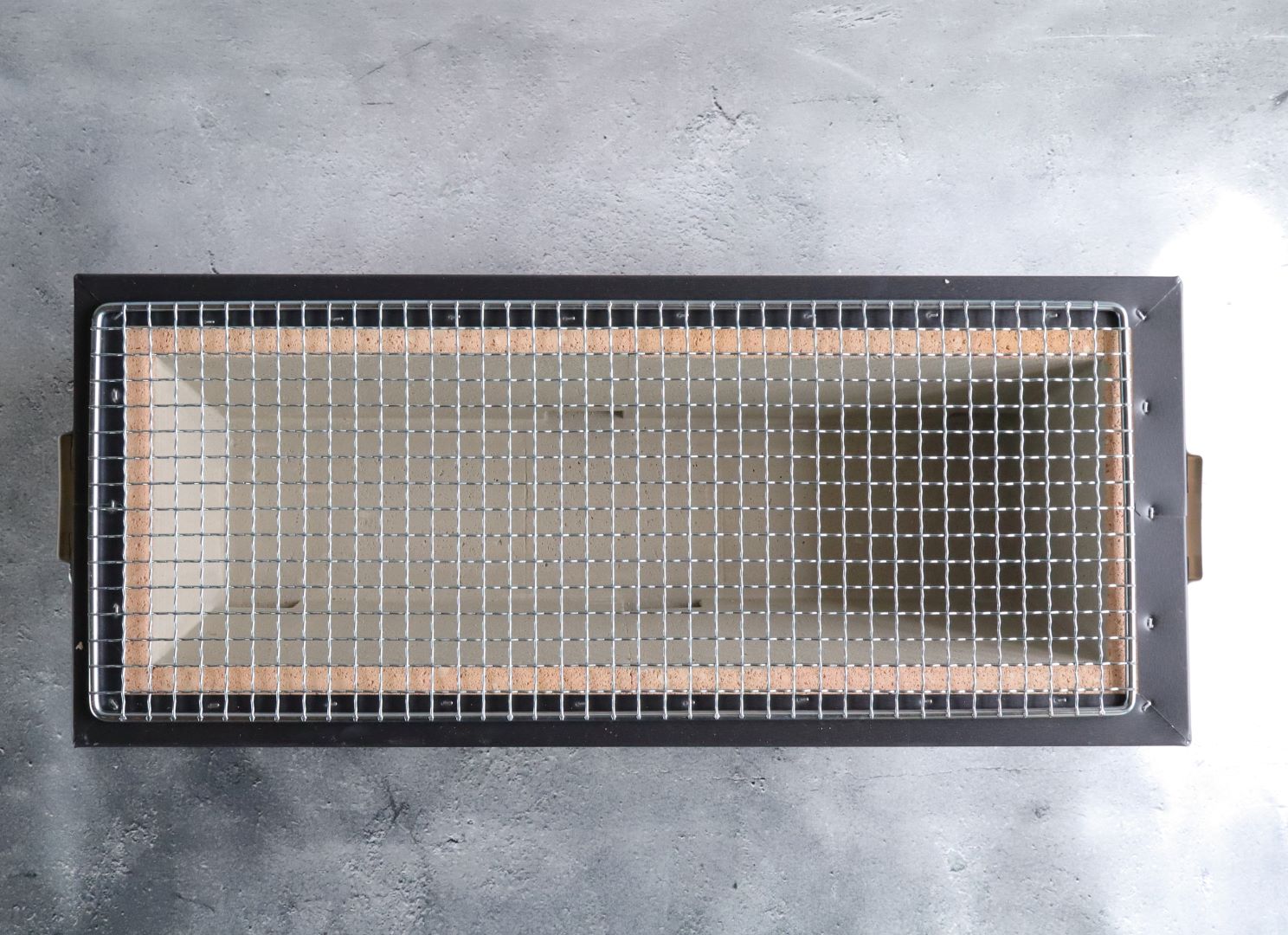 A top view of a Japanese hibachi grill with a metal grate, ready for grilling, with cork insulation and metal framing.