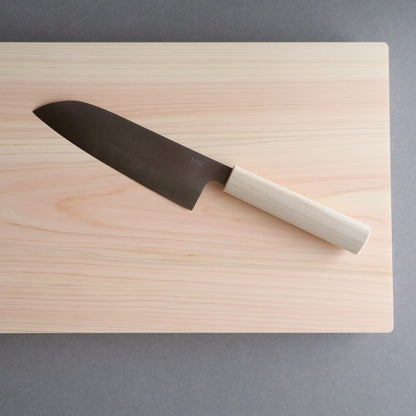 A Japanese Santoku knife with a light wooden handle placed on a wooden cutting board, showcasing a minimalist and traditional design.