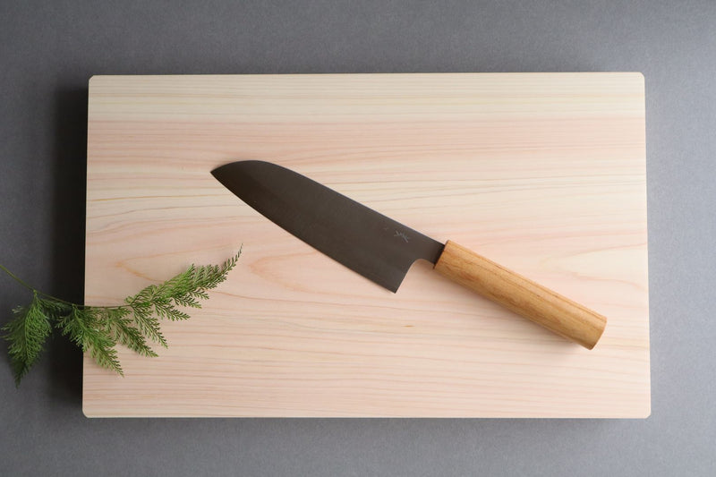 A Japanese Santoku knife with a brown wooden handle resting on a wooden cutting board, accompanied by a sprig of greenery.