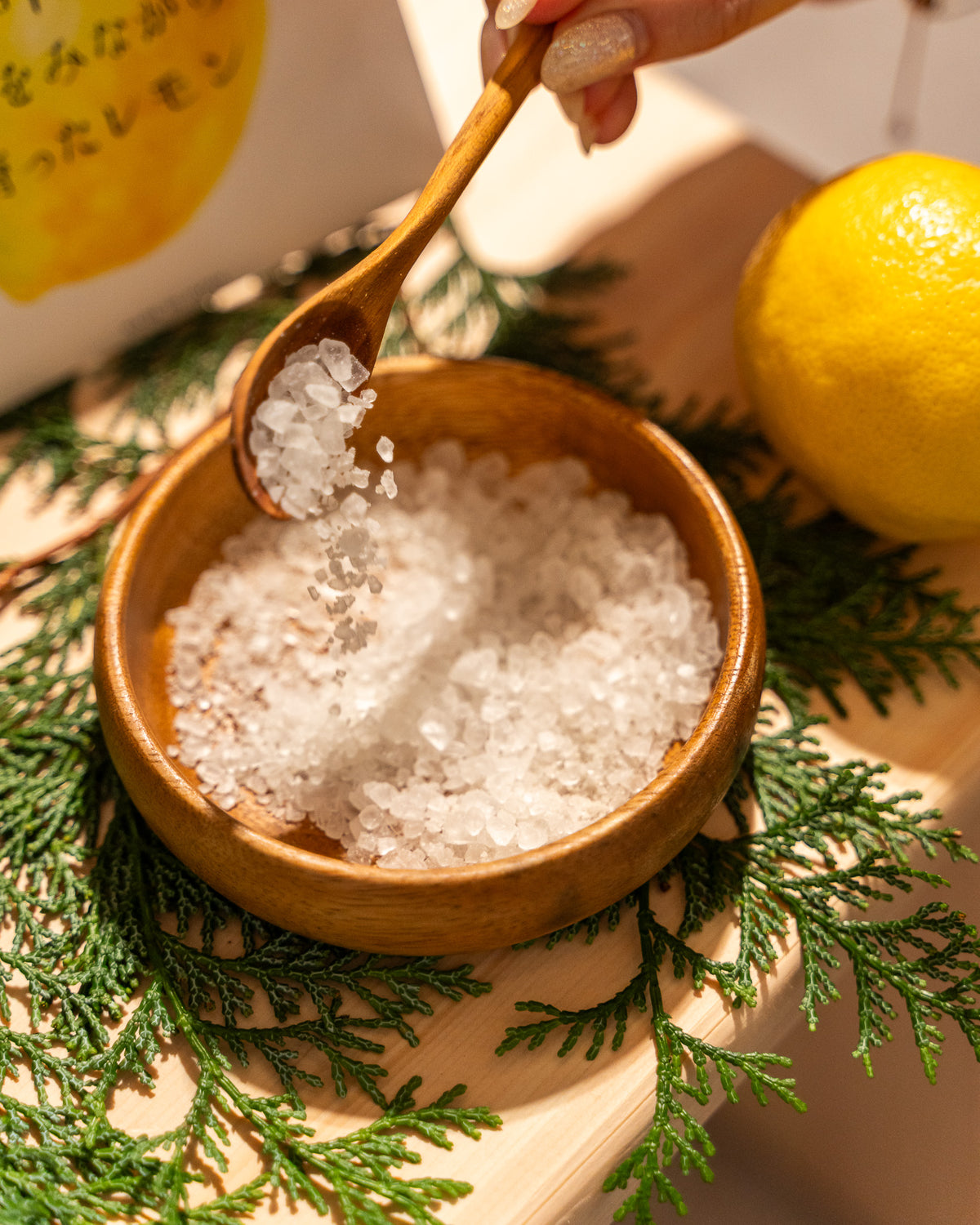 Wooden bowl filled with sea salt, a wooden spoon, and a lemon on a decorative surface.
