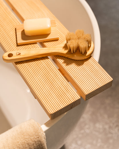 Wooden bath brush, scrubber, and soap on a wooden tray with a neutral background