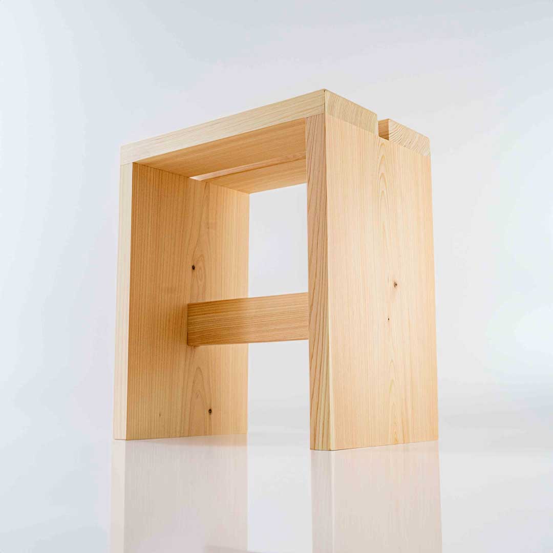 A rectangular wooden bath stool placed in a white bathroom with reflection on the floor
