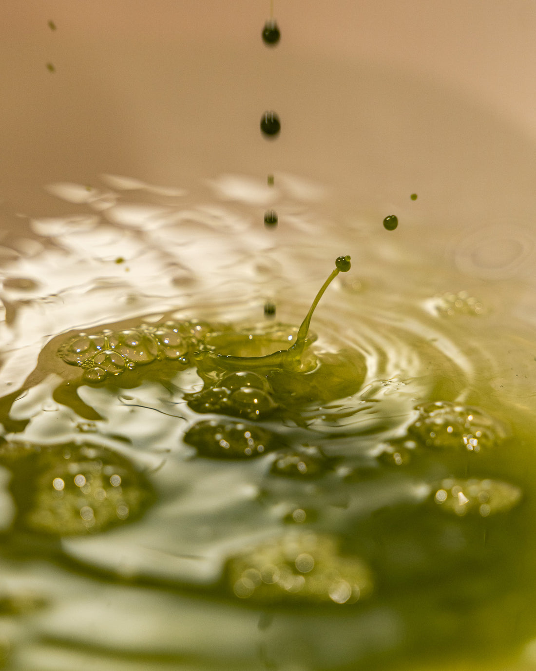 Close-up of a green droplet splashing into water with ripples.