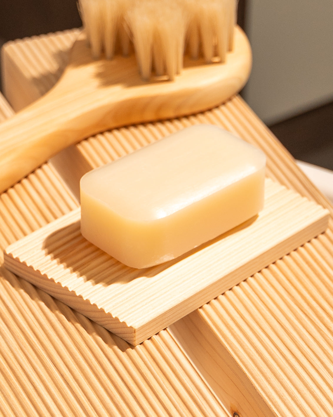 Bar of soap on a wooden soap dish with a brush in the background
