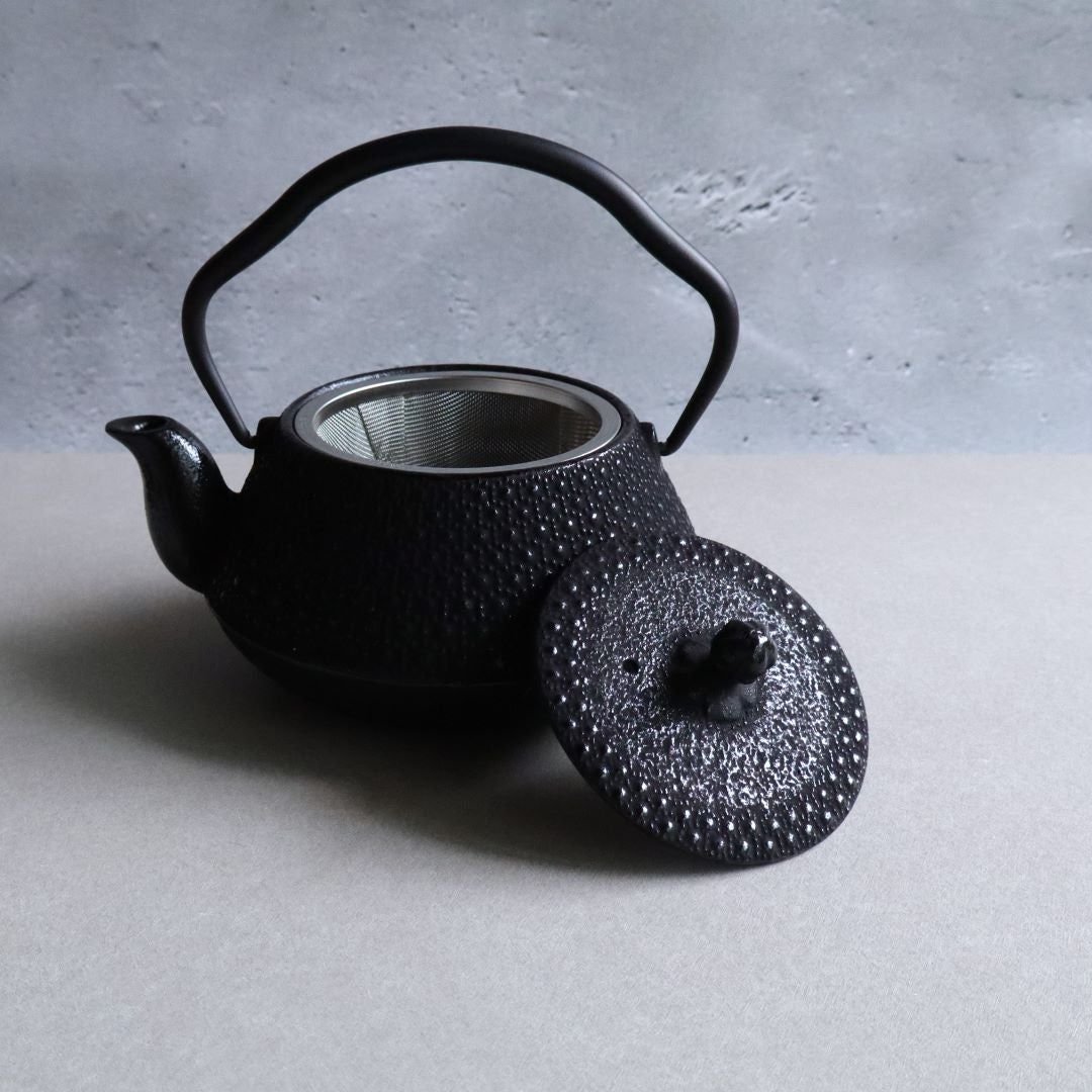 A Nambu Tekki teapot with the lid removed, showcasing the stainless steel mesh strainer inside. The teapot features a traditional hexagonal pattern and a curved handle, all set against a neutral background.