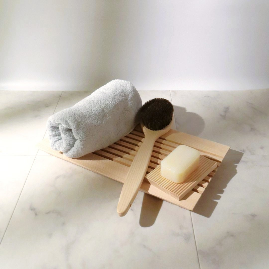 Hinoki wood bath mat with folded towel, wooden body brush, and soap on marble surface in soft natural light