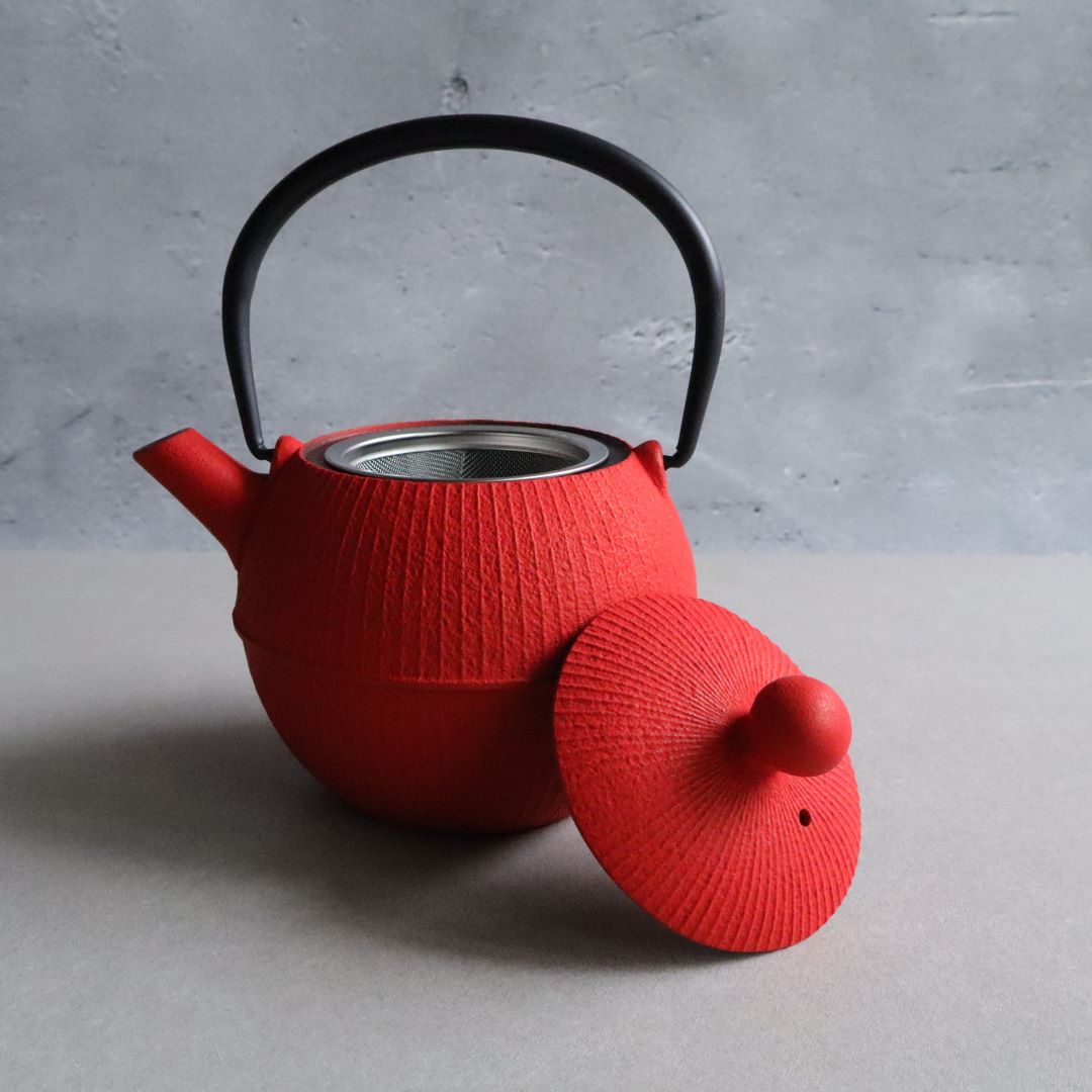 A red Nambu Tekki teapot with the lid removed, revealing the stainless steel mesh strainer inside. The teapot is set against a neutral background, highlighting its unique temari shape and vibrant color.
