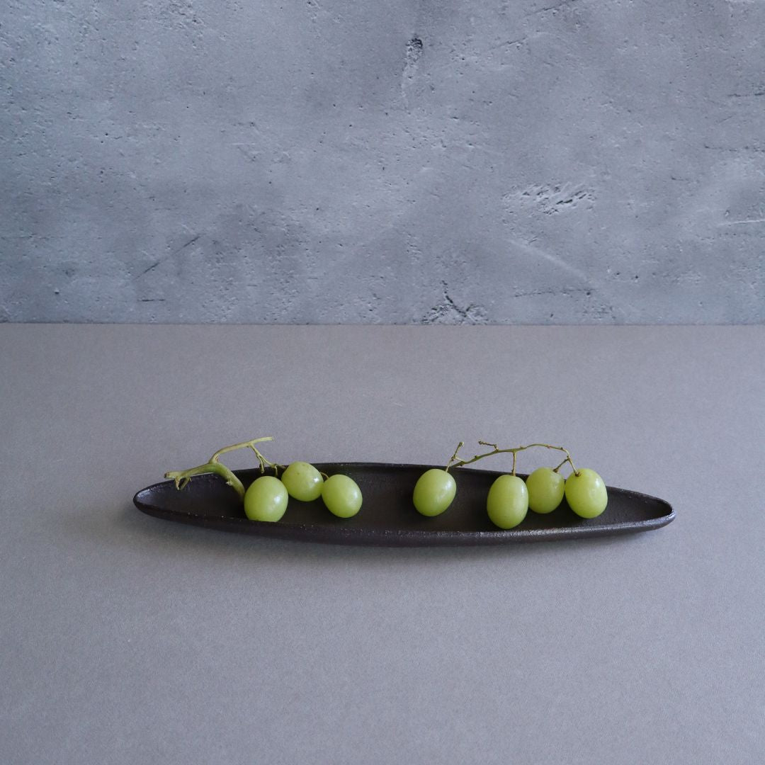 Green grapes on a black oval plate against a gray background