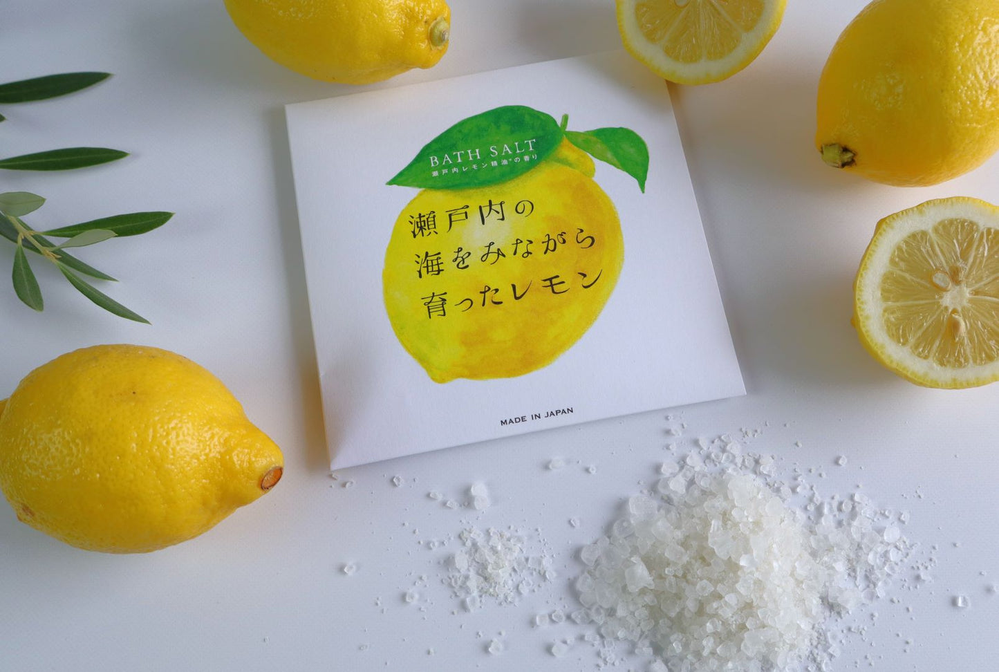 A packet of Setouchi Lemon Bath Salt placed next to coarse sea salt crystals and fresh lemons, highlighting the natural ingredients.