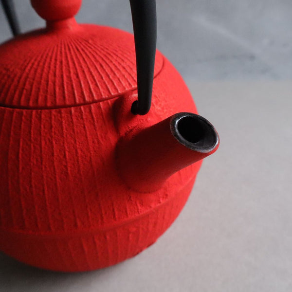 Close-up view of the spout of a red Nambu Tekki teapot, showcasing the intricate design and craftsmanship. The teapot is shaped like a traditional Japanese temari ball and features a black handle.