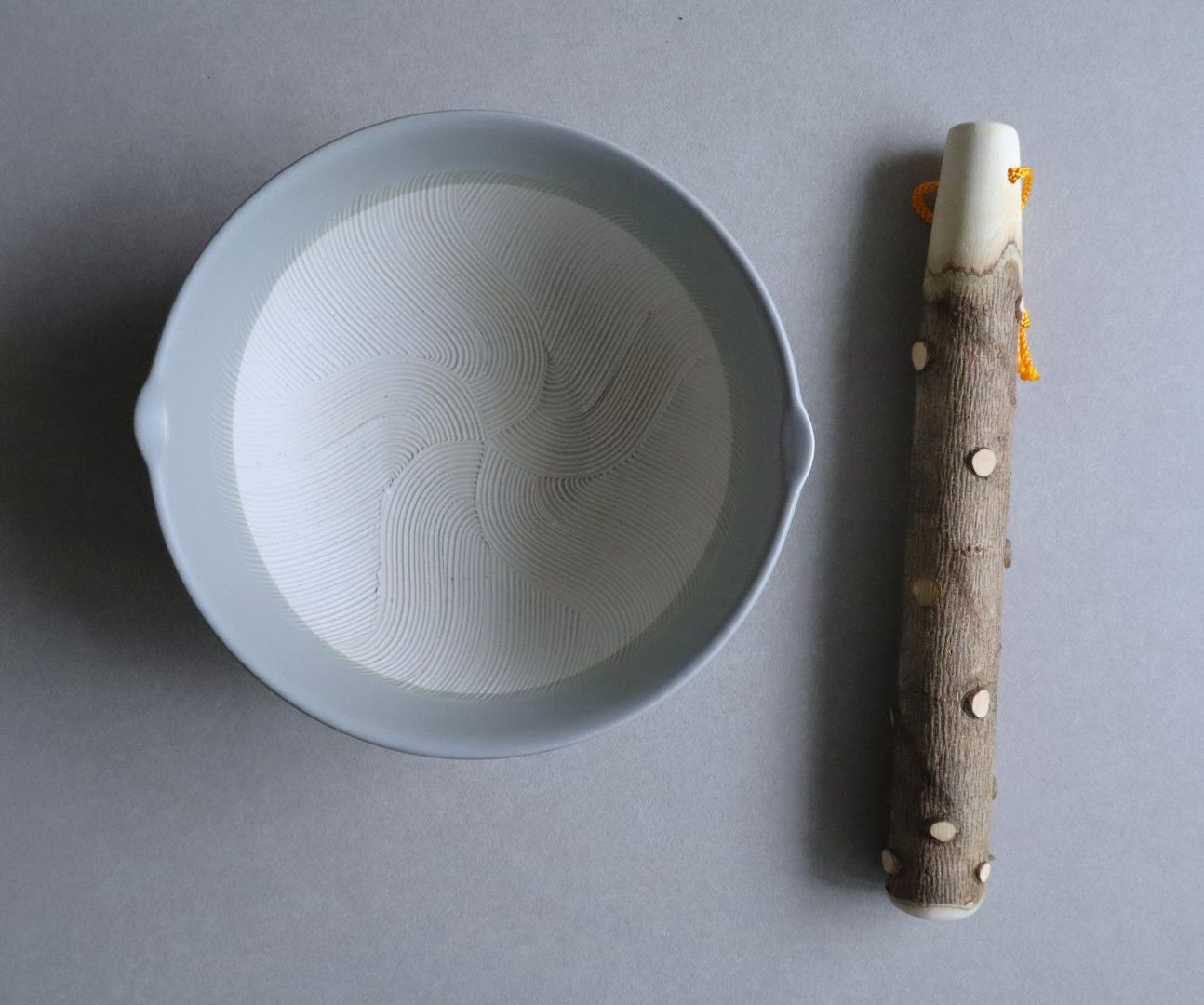 Overhead view of a ceramic suribachi and a sansho wood pestle placed side by side