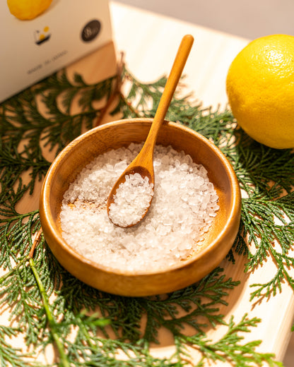 Wooden bowl with sea salt and a wooden spoon on a green leafy background