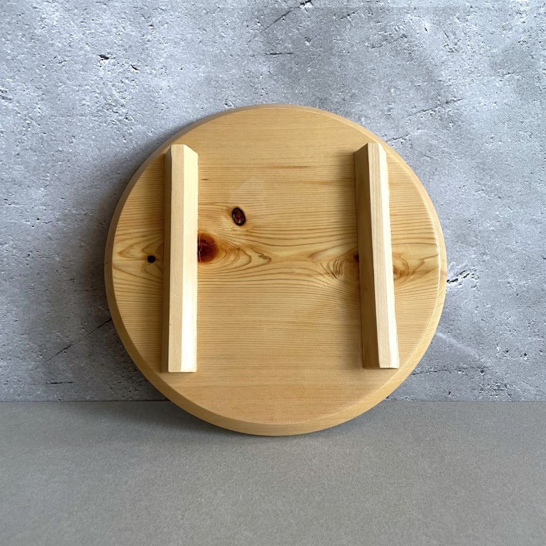 Back view of a round wooden sushi plate against a grey wall background.