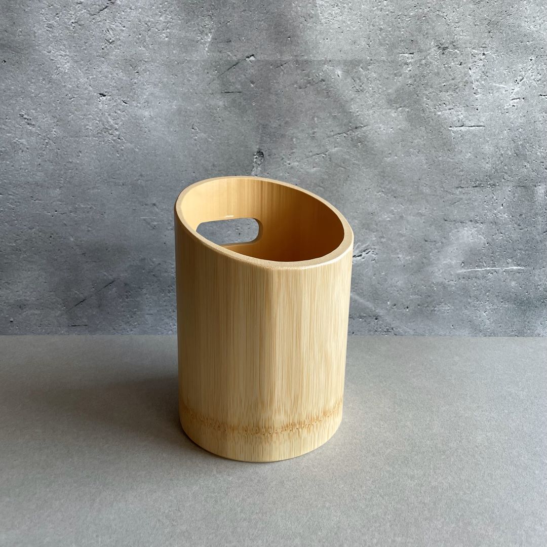 A light wooden wine cooler with a handle cutout, standing on a gray surface with a textured concrete wall in the background.