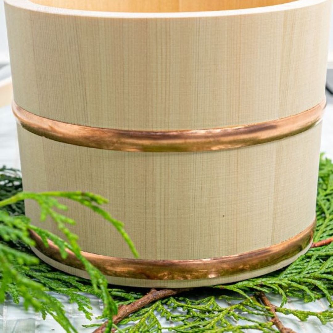 A Japanese wooden bath bucket with handle on a pine branch inside a white bathroom floor