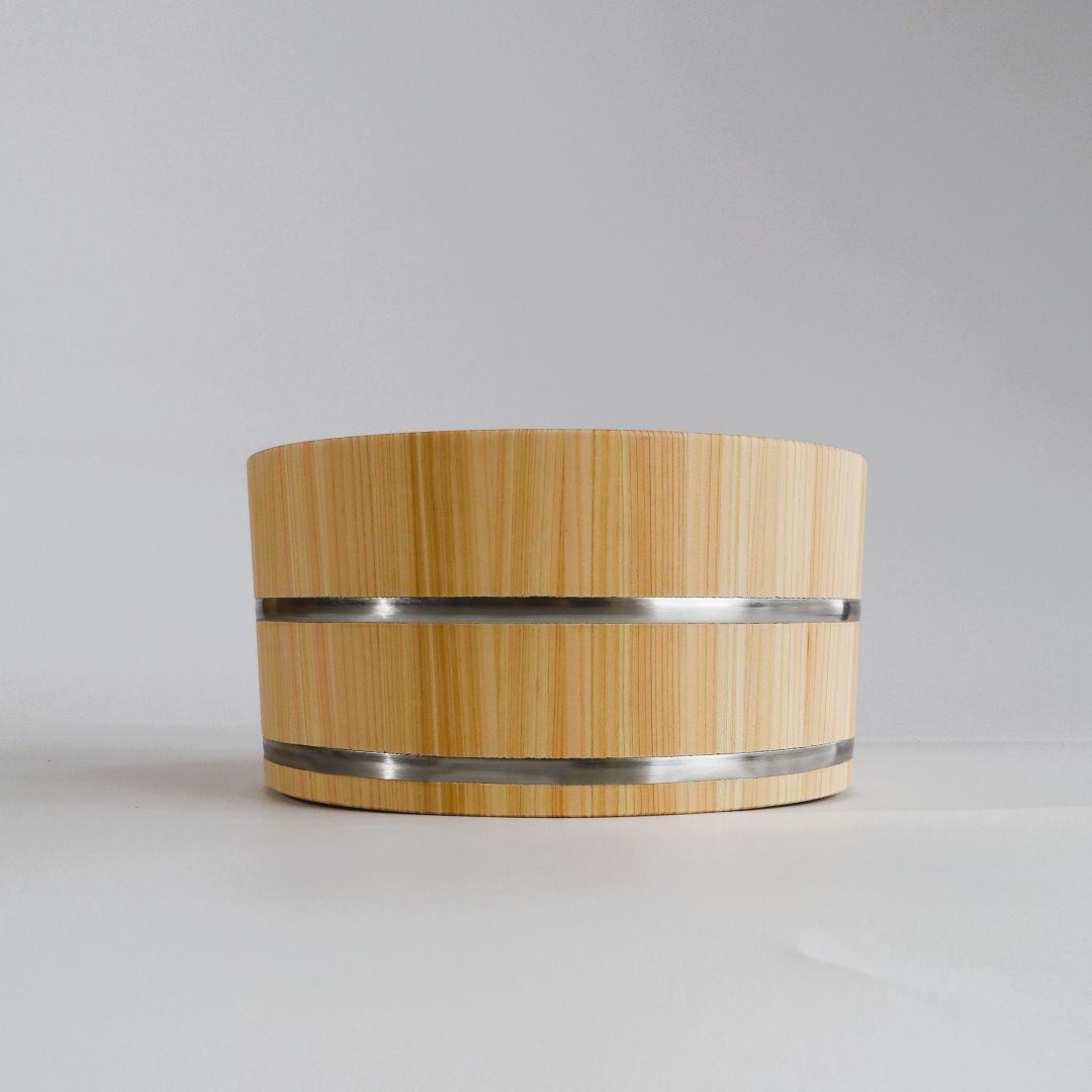 A light natural bamboo or wood bucket with two horizontal silver metal bands, photographed against a neutral light gray background.