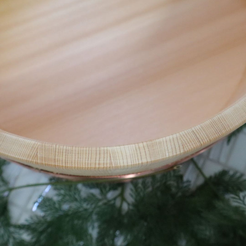 Close-up of the smooth interior and detailed wood grain of a φ22cm / 8.66" Sawara Japanese cypress bath bucket, with a hint of copper banding and soft green ferns in the background.