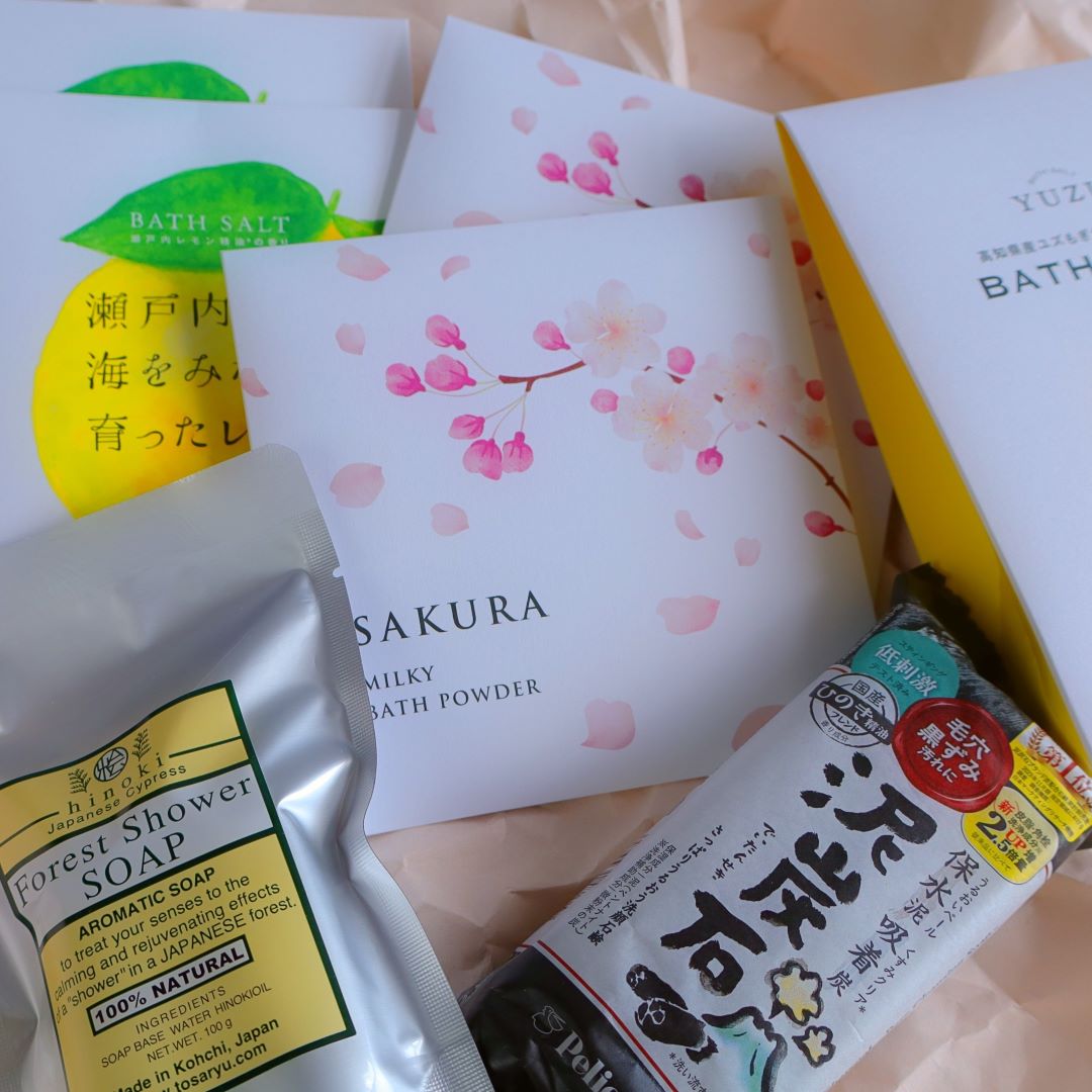 Japanese bath and body care products, including Sakura Milky Bath Powder, Yuzu Bath Salt, Setouchi Lemon Bath Salt, Forest Shower Soap with Hinoki, and a Japanese charcoal soap bar, arranged on soft wrapping paper.