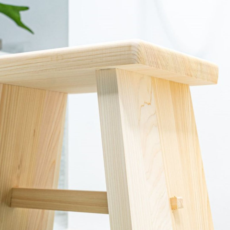 A Japanese wooden bath stool is placed in the middle of a bathroom with white faience tiles covering the walls. The stool is positioned next to a bath and there are green plants on the bath, adding a natural touch to the bathroom decor.