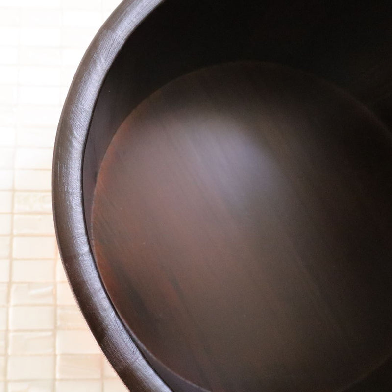 Close-up of a black Hinoki Cypress bucket interior, showcasing the smooth wood grain and dark finish, with the tiled floor in the background providing a contrasting texture.