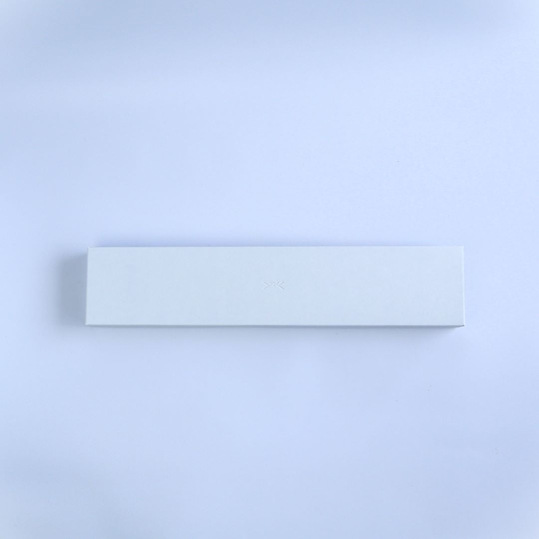 A minimalist white rectangular knife box on a soft white background, with the maker's subtle logo embossed in the center, suggesting elegance and simplicity.