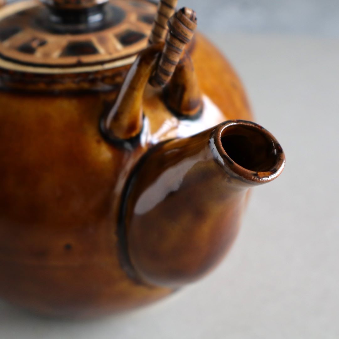 Close-up of the spout of a handmade Japanese ceramic teapot with a warm brown glaze. The glossy finish and smooth curves highlight the traditional craftsmanship, making it a beautiful and functional piece for tea brewing.