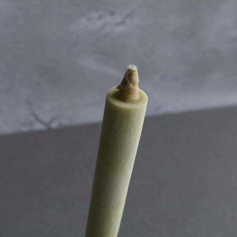 Top section of a Japanese sumac wax taper candle showing the wick, with a blurred gray and white background emphasizing the candle&#39;s texture and natural color.