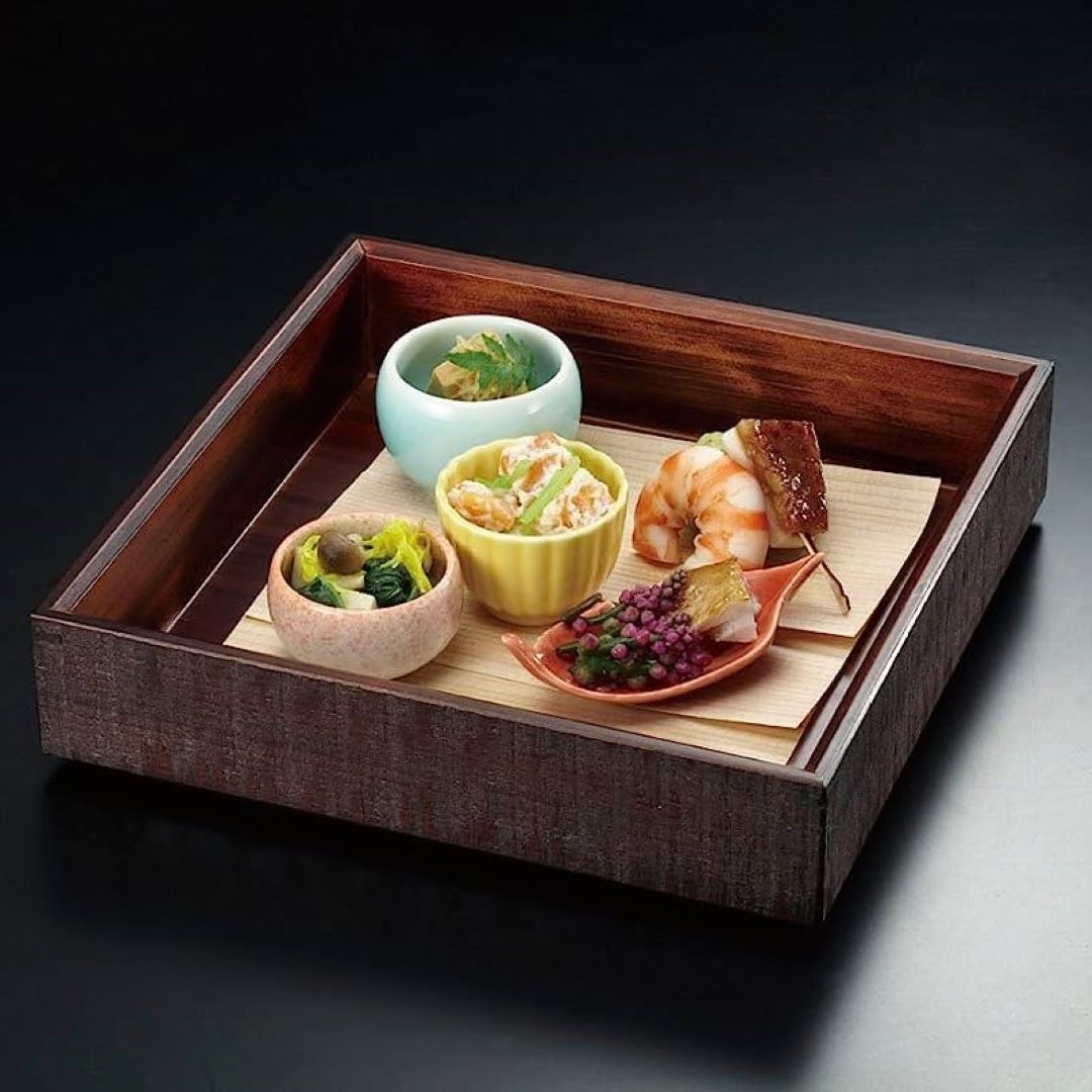 a traditional bento lunch box with four small dishes on a wooden sheet