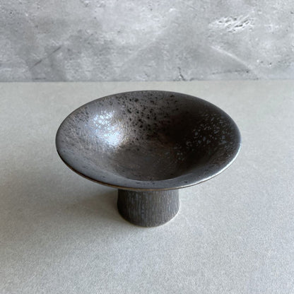 A round black ceramic plate with a visible in front a grey wall