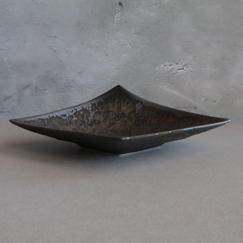 Side view of a Japanese porcelain tray on a gray background. The tray has an angular design with a metallic glaze that includes mottled patterns of gray, black, and blue. Its elevated edges give it a dynamic, sculptural quality.