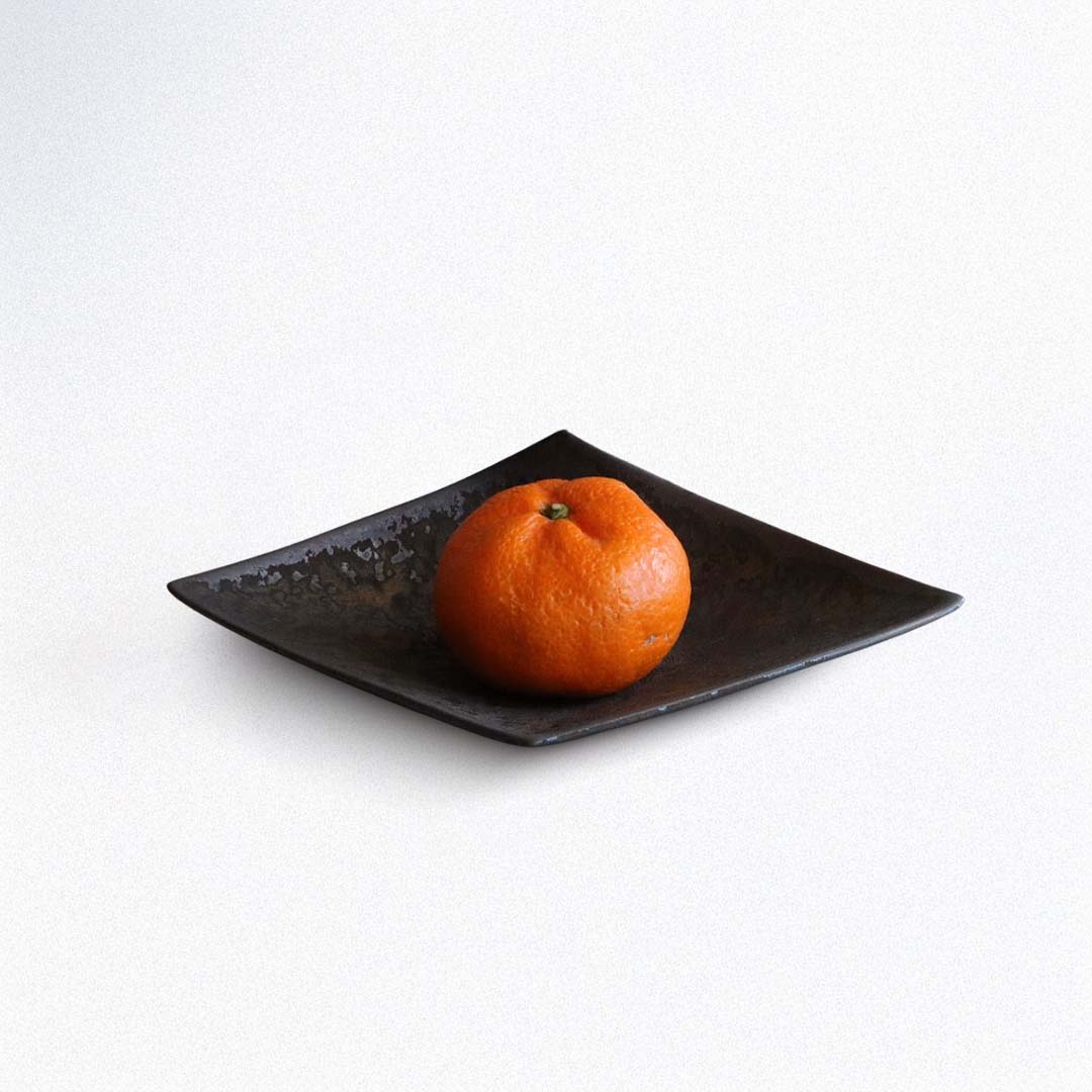 Orange on a dark square plate on a white background